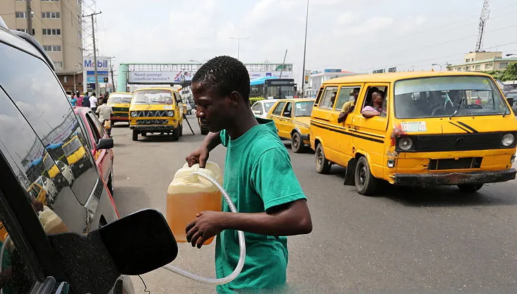 A man fills an automobile with fuel sold on the black market as others queue to buy fuel on a major road. Photographer: George Osodi/Bloomberg