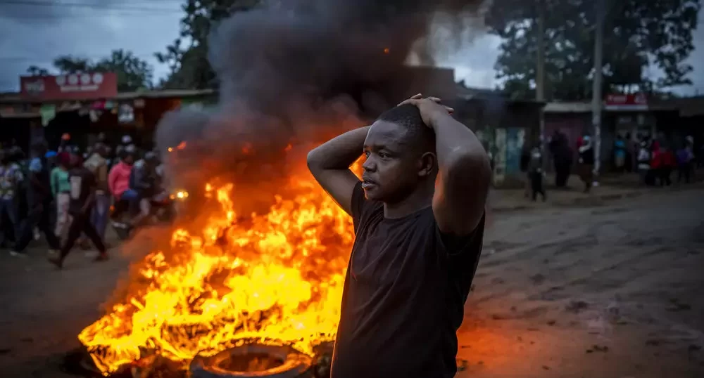 A supporter of presidential candidate, Raila Odinga stands next to a barrage of burning tires in the Kibera neighborhood of Nairobi, Kenya, Monday, Aug. 15, 2022.